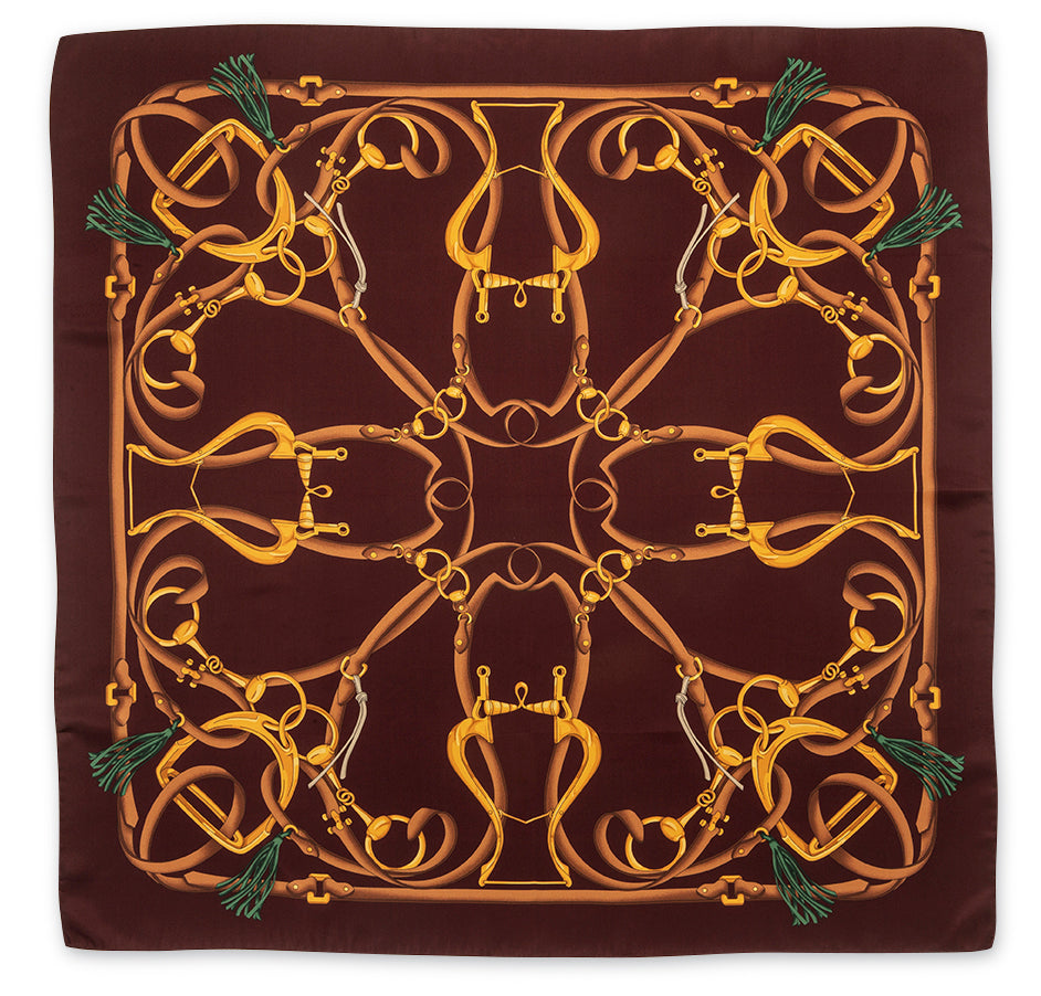 A square silk scarf featuring an intricate equestrian design with golden horse bits and reins on a dark brown background, finished with green tassels in the corners.