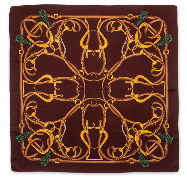 A square silk scarf featuring an intricate equestrian design with golden horse bits and reins on a dark brown background, finished with green tassels in the corners.