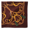 A square silk scarf featuring an intricate equestrian design of golden horse bits and reins over a deep burgundy background, finished with green tassels at the corners.