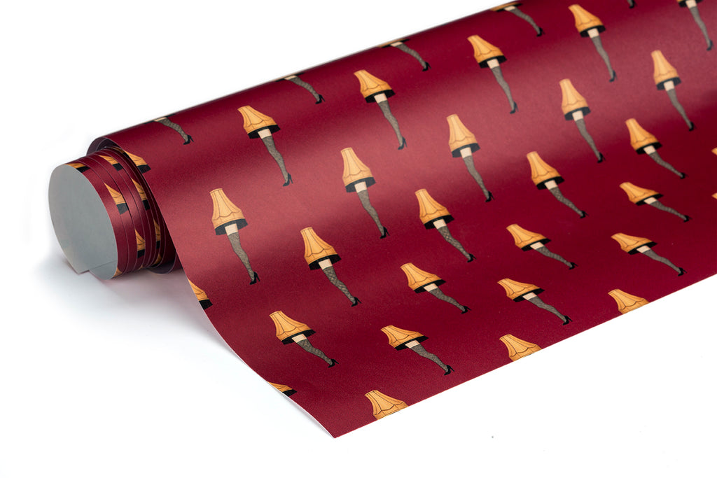 A roll of wrapping paper featuring a repeating pattern of classic Christmas leg lamps on a deep red background, with the roll positioned diagonally across the frame.